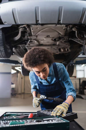 young african american mechanic standing beneath lifted car in garageの写真素材