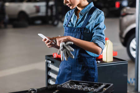 partial view of young african american mechanic typing on cellphone in garageの写真素材