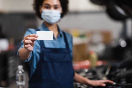 empty card in hand of blurred young african american mechanic in protective mask in garage