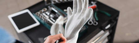 cropped view of young mechanic wearing glove on hand near toolbox and digital tablet in garage, bannerの写真素材