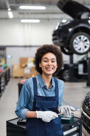 smiling young african american mechanic holding wrench in garage