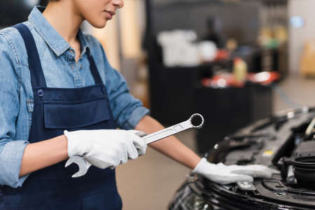 partial view of young african american mechanic holding wrench near car hood in garageの写真素材