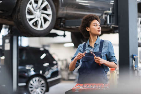 young african american mechanic holding equipment near toolbox in garage