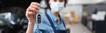 close up view of car key in hand of blurred young african american mechanic in protective mask in garage, bannerの写真素材