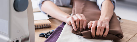 Cropped view of seamstress taking cloth near scissors and sewing machine, bannerの写真素材
