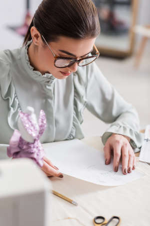 Designer looking at sketches near mannequin and cloth on blurred foregroundの写真素材