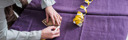 Cropped view of seamstress marking cloth near tape measure, banner