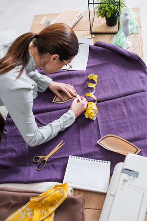 High angle view of designer with sewing pattern marking cloth on tableの写真素材