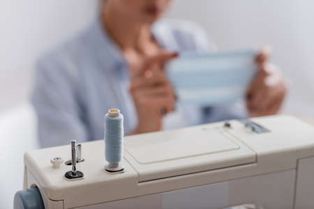 Cropped view of thread on sewing machine near blurred seamstress