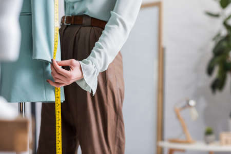 Cropped view of seamstress with tape measure near blurred blazer
