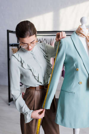 Designer measuring sleeve of blazer on mannequin while working in atelierの写真素材