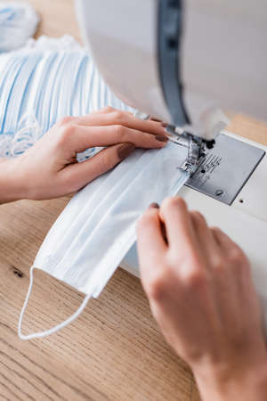 Cropped view of seamstress sewing medical mask on blurred machine