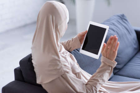 muslim woman waving hand during video call on digital tablet at homeの写真素材