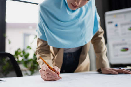 cropped view of blurred muslim engineer drawing blueprint in officeの写真素材