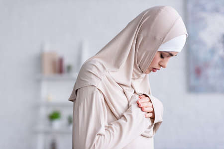 young muslim woman holding hands on chest while praying with closed eyesの写真素材