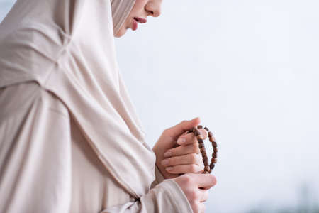 partial view of young arabian woman holding rosary during pray at homeの写真素材