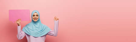 happy muslim woman with blue speech bubble looking at camera on pink background, bannerの写真素材