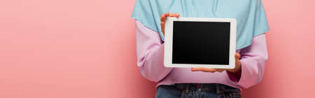 partial view of muslim woman holding digital tablet with blank screen on pink, bannerの写真素材