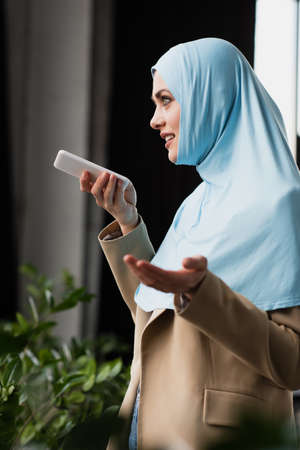 pretty muslim businesswoman gesturing while sending voice message on smartphone