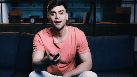 happy man holding remote controller and clicking channels at homeの写真素材