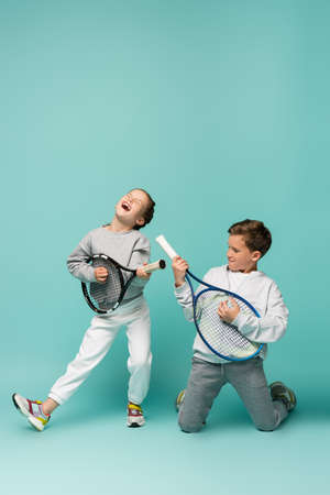 amazed kids holding tennis rackets while singing and pretending performing on blueの写真素材