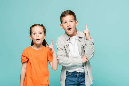 excited kids pointing up with fingers while having idea isolated on blueの写真素材