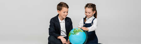happy schoolgirl and schoolboy looking at globe isolated on gray, bannerの写真素材
