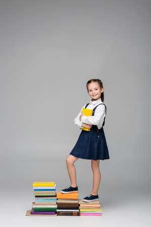 happy schoolgirl standing on pile of books on grayの写真素材