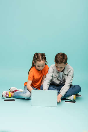 kids using laptop near smartphones with blank screen on blueの写真素材