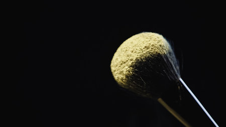 yellow holi paint on soft cosmetic brush isolated on blackの写真素材