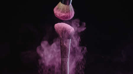 soft cosmetic brushes making splashes of pink holi paint on black backgroundの写真素材