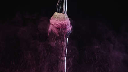 cosmetic brushes hitting and making splashes of colorful purple holi paint on black backgroundの写真素材