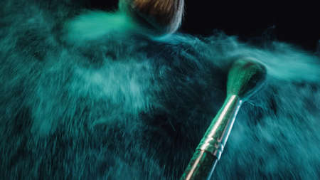 soft cosmetic brushes making splashes of turquoise dust on black backgroundの写真素材