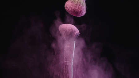 soft cosmetic brushes near splashes of pink dust on black backgroundの写真素材