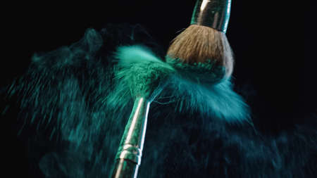 cosmetic brushes making splashes of blue powder on black backgroundの写真素材