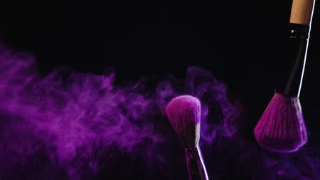 soft cosmetic brushes with purple powder near dust splashing on black backgroundの写真素材