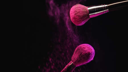 cosmetic brushes with bright pink holi powder near dust splashing on black backgroundの写真素材