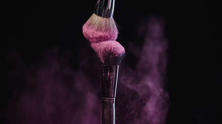 soft cosmetic brushes with pink holi powder near color dust on blackの写真素材