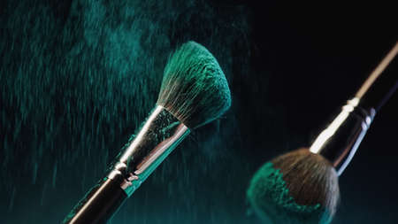 cosmetic brushes with bright turquoise holi paint near dust splash on black backgroundの写真素材