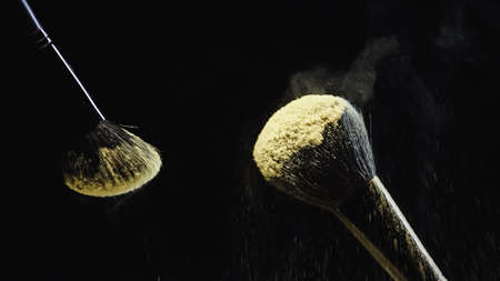 cosmetic brushes with yellow holi powder on black backgroundの写真素材