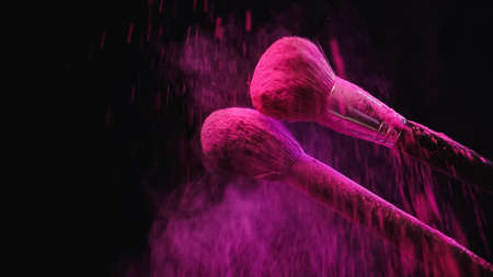 soft cosmetic brushes making explosion of pink powder on black backgroundの写真素材