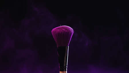 cosmetic brush with purple holi powder near dust on black backgroundの写真素材