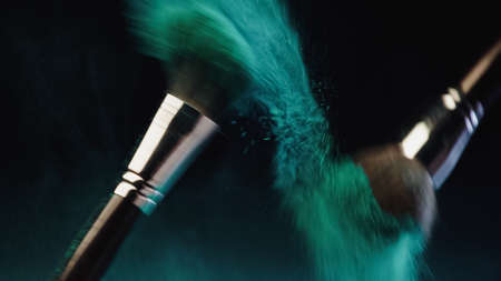 blurred cosmetic brushes with vibrant turquoise holi paint splashing on black backgroundの写真素材