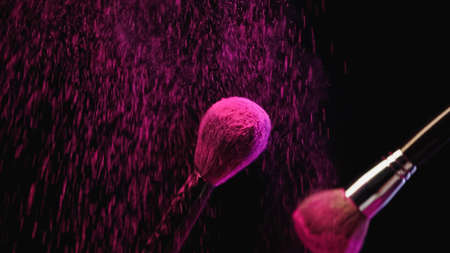 cosmetic brushes with pink holi powder near dust splashing on black backgroundの写真素材