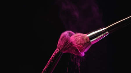 cosmetic brushes with bright pink holi powder hitting on black background