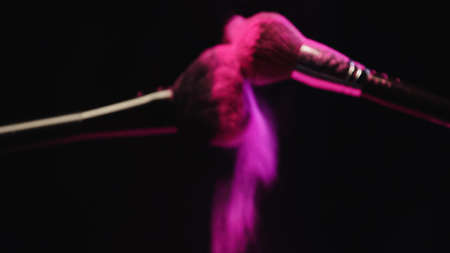 blurred cosmetic brushes making explosion of pink powder on black backgroundの写真素材