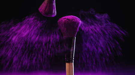 bright cosmetic brushes with holi paint near pink dust on black backgroundの写真素材
