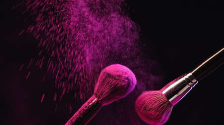 cosmetic brushes with bright pink powder splashing on black backgroundの写真素材