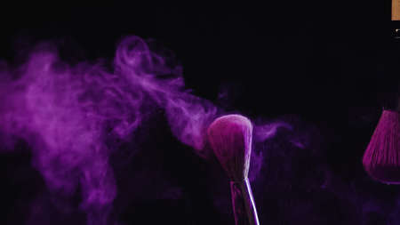 cosmetic brushes with vibrant purple holi paint near dust splashing on black backgroundの写真素材