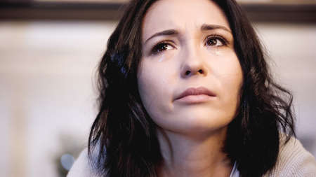 close up view of upset woman crying with tears and looking up at homeの写真素材